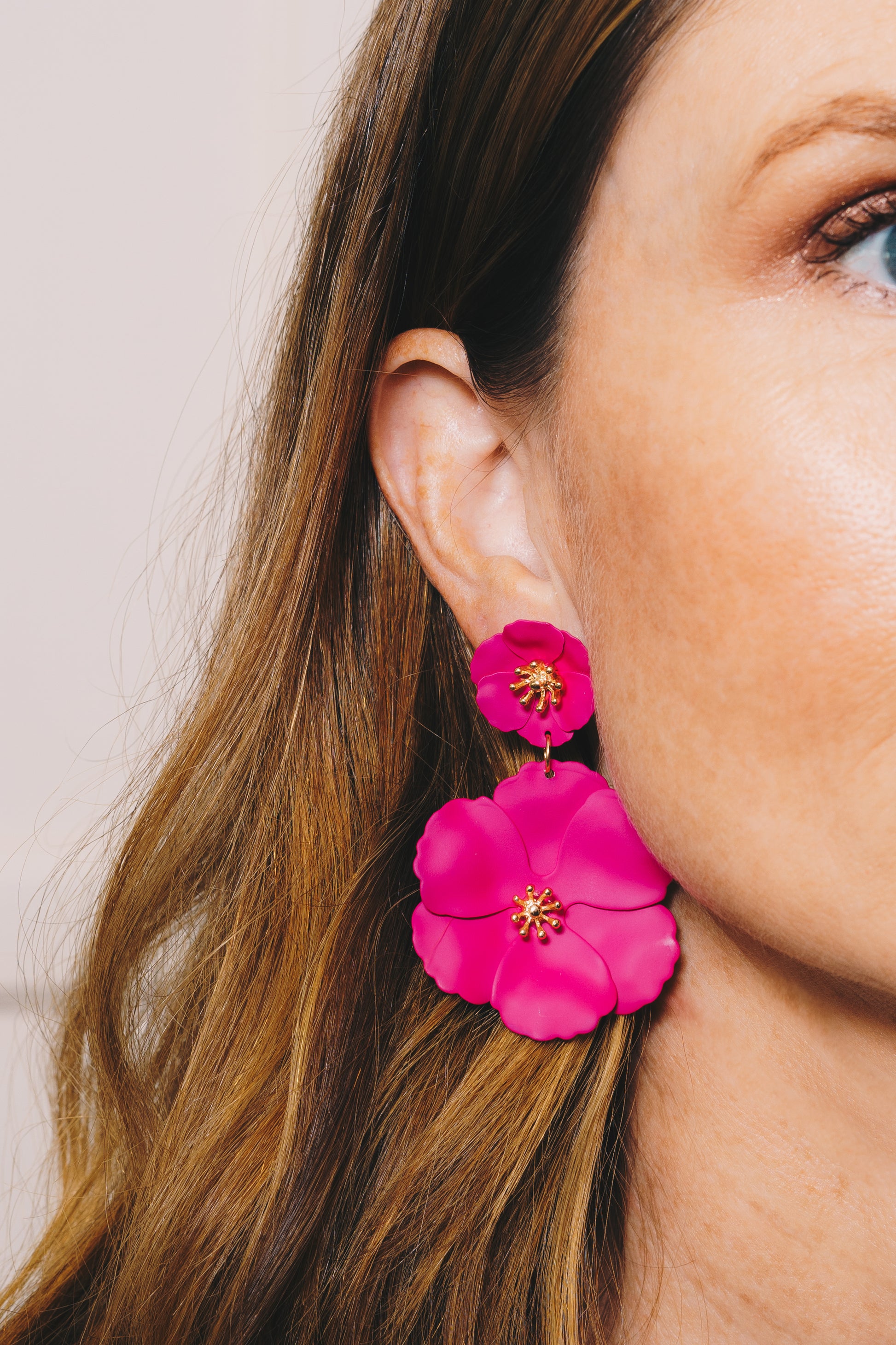 close up of model wearing bright pink enamel flower drop earrings
