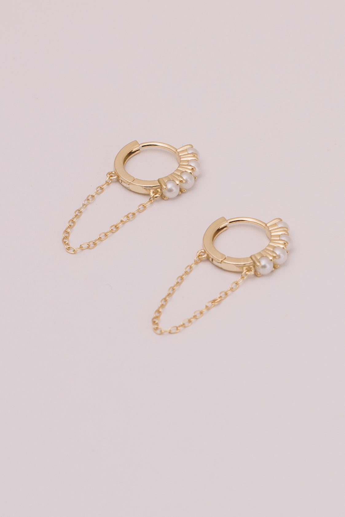 pearl and gold huggie hoop earrings with chain dangles on white background