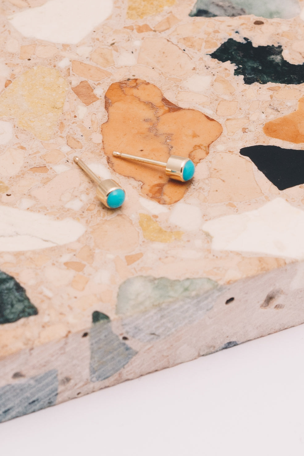 turquoise and gold bezel set stud earrings on multicolored marble
