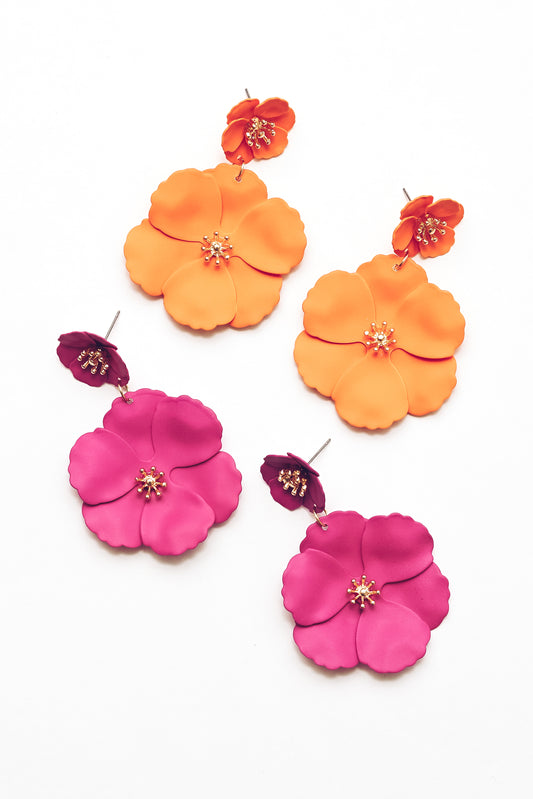 Close-up of bright orange enamel flower drop earrings and pink flower enamel earrings