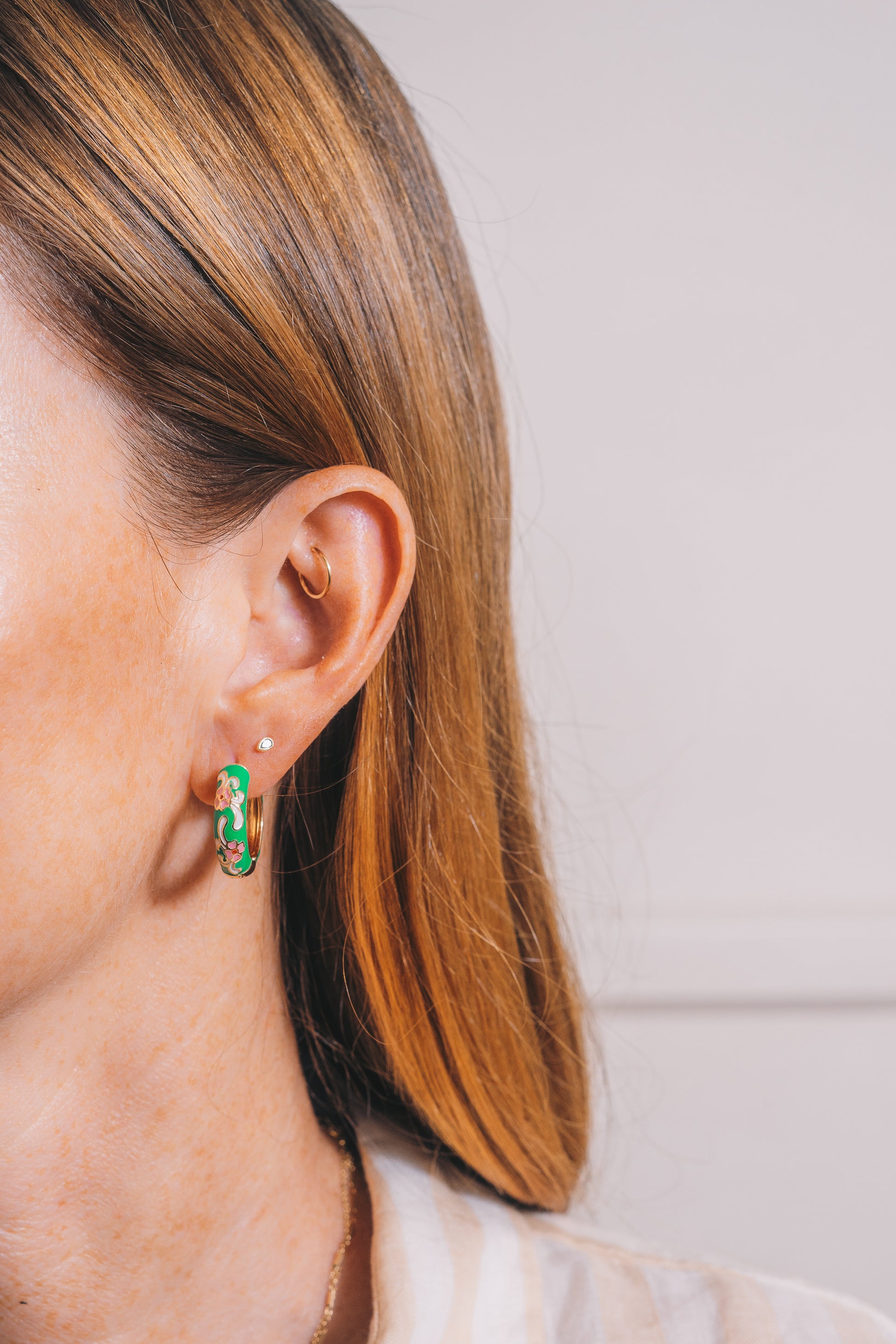 green cloisonné huggie hoop earrings on red haired model with multiple piercings