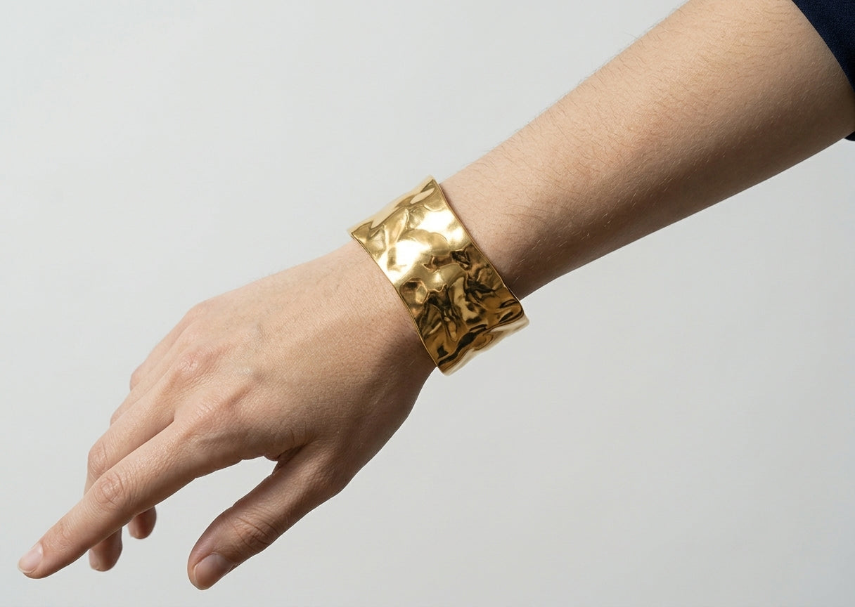 Gold bracelet on a wrist against a plain background