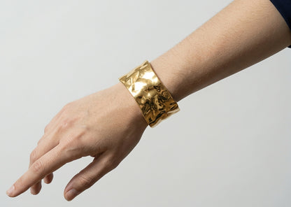 Gold bracelet on a wrist against a plain background