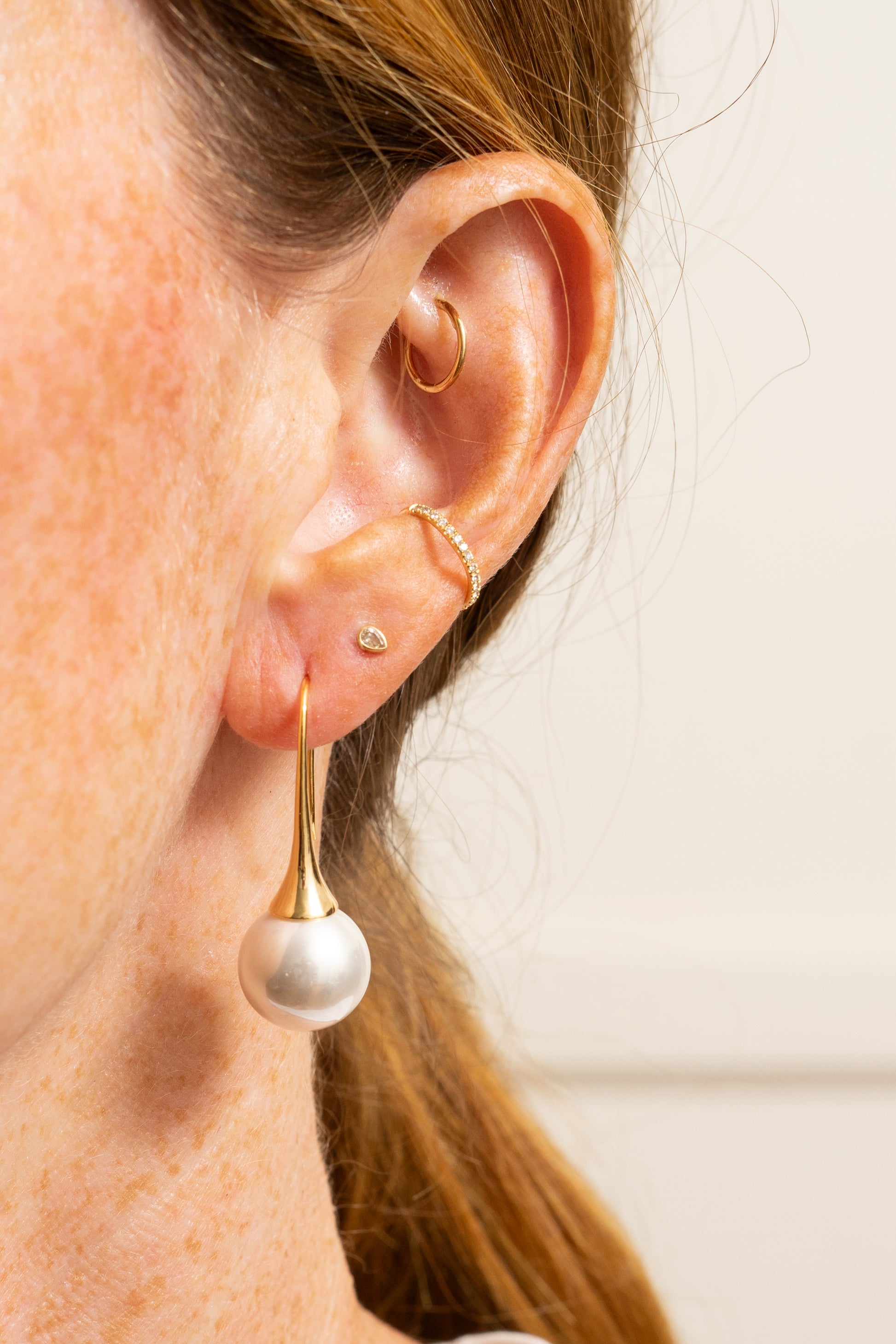 minimal pearl drop earrings with long gold earwires on model with multiple ear piercings closeup