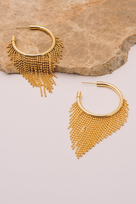 gold fringe hoop chain earrings on tan marble and white background