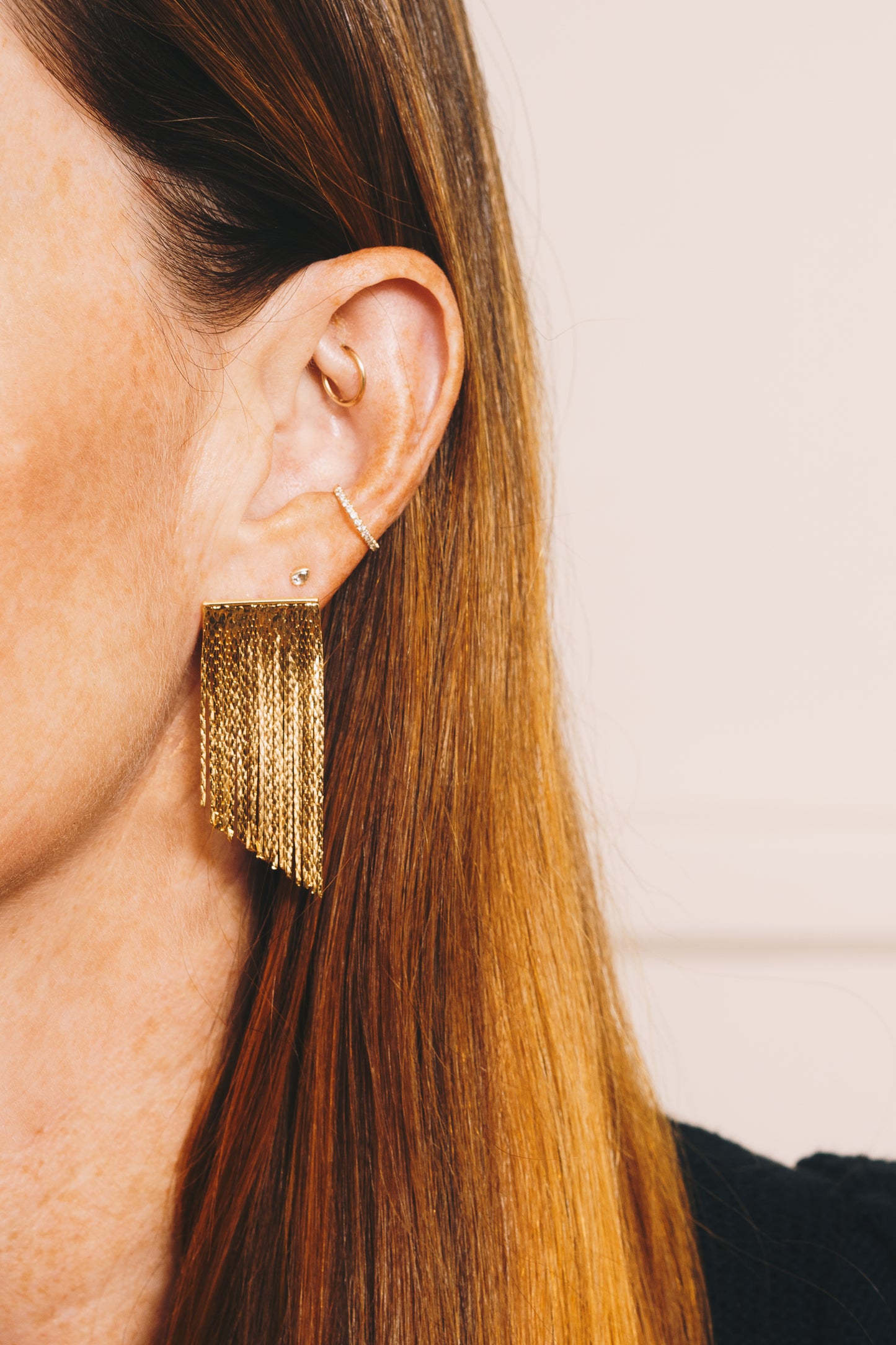 gold fringe chain earrings on red haired model with multiple ear piercings closeup