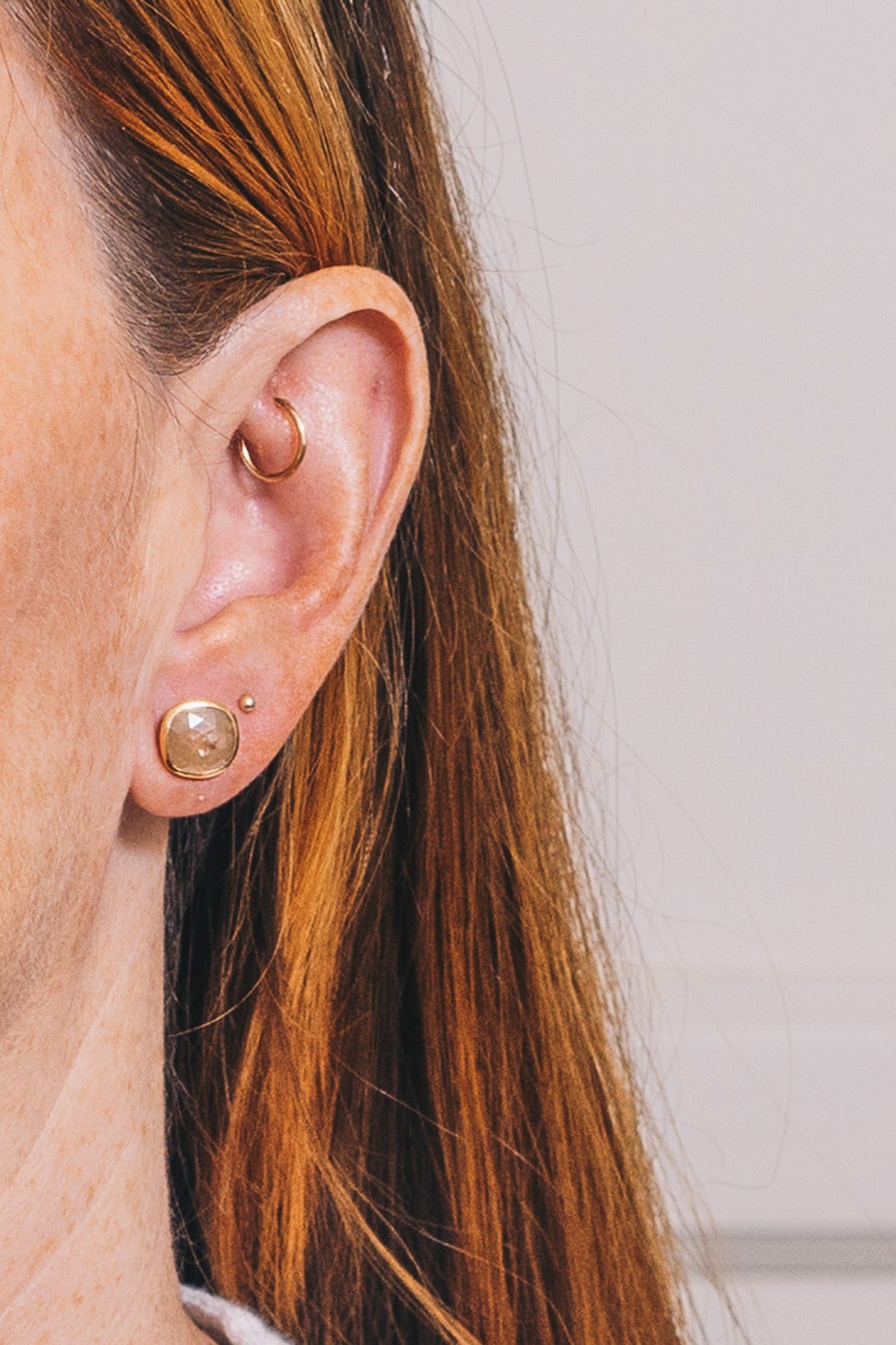 raw diamond stud earrings on red haired model with multiple piercings closeup