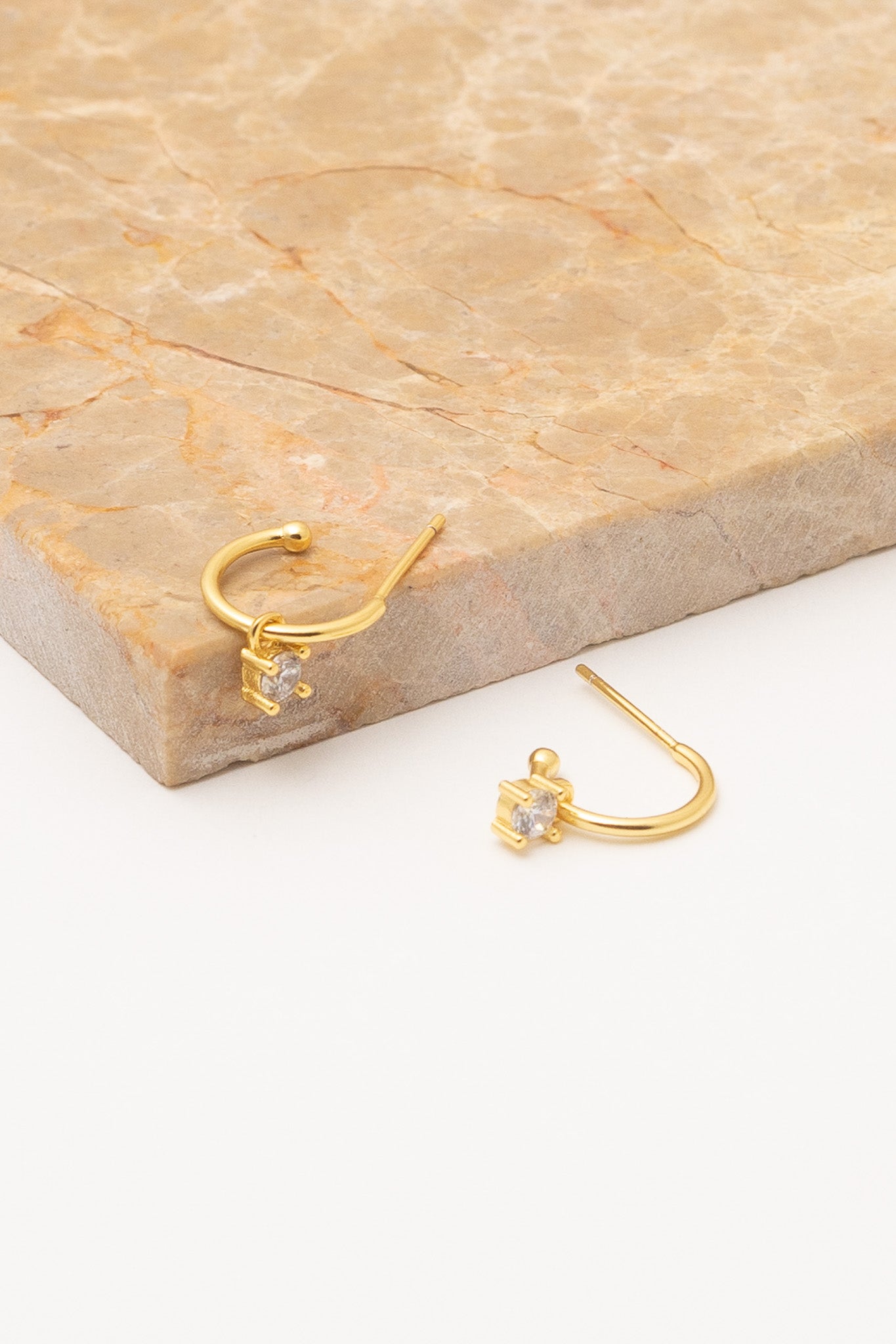 small gold hoops with crystal dangles on tan marble background closeup