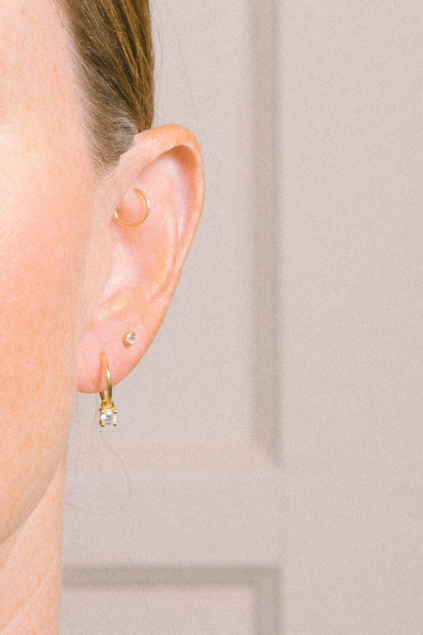 tiny gold hoop with crystal dangle on model with multiple piercings close-up 