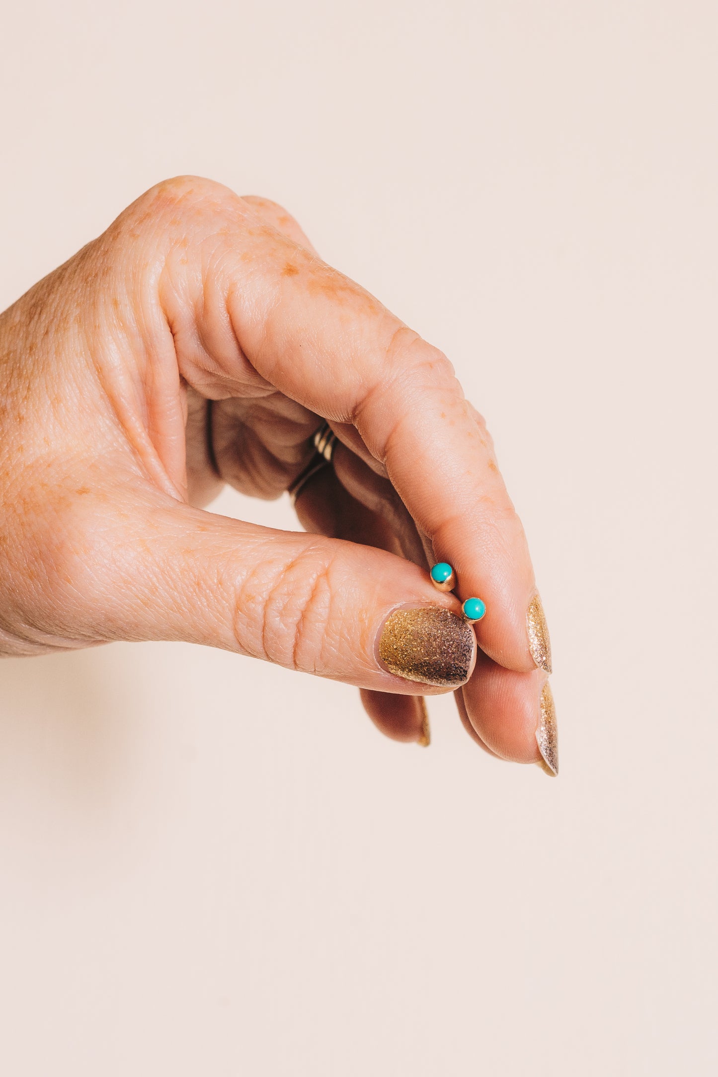 hand holding tiny turquoise bezel set stud earrings between fingers